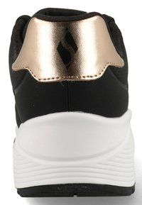 Baskets noires avec une tige texturée, un onglet de talon doré métallisé et une semelle en caoutchouc blanche ; présente des perforations pour la respirabilité.