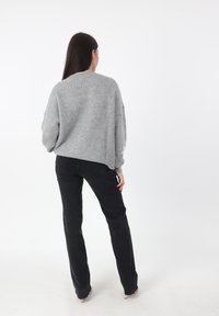 Maglione grigio lavorato a maglia con vestibilità ampia e texture a coste, abbinato a jeans neri attillati. La vista mostra il retro dell'outfit.