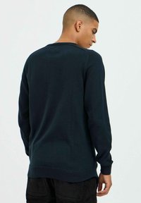 Sweatshirt à col rond de couleur bleu foncé avec des manches longues, des poignets et un ourlet côtelés, présentant une texture douce et lisse.