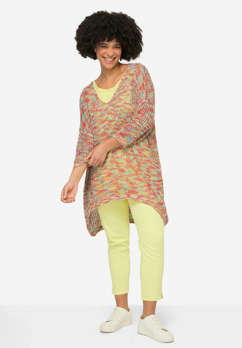 Multikleuren gebreide tuniek met een V-hals, driekwartmouwen en een hoge-laag zoom. Gepaard met lichtgele slim fit broek en witte sneakers.
