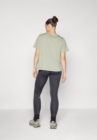 Ljusgrön bomullströja med korta ärmar, kombinerad med svarta leggings och grå sportskor. Tyget verkar mjukt och slätt.