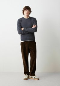 Pullover: grigio scuro, maglia, collo a giro, maniche lunghe. Pantaloni: corduroy marrone, vestibilità ampia. Calzature: beige con accenti grigi, suola stratificata. Senza loghi visibili.