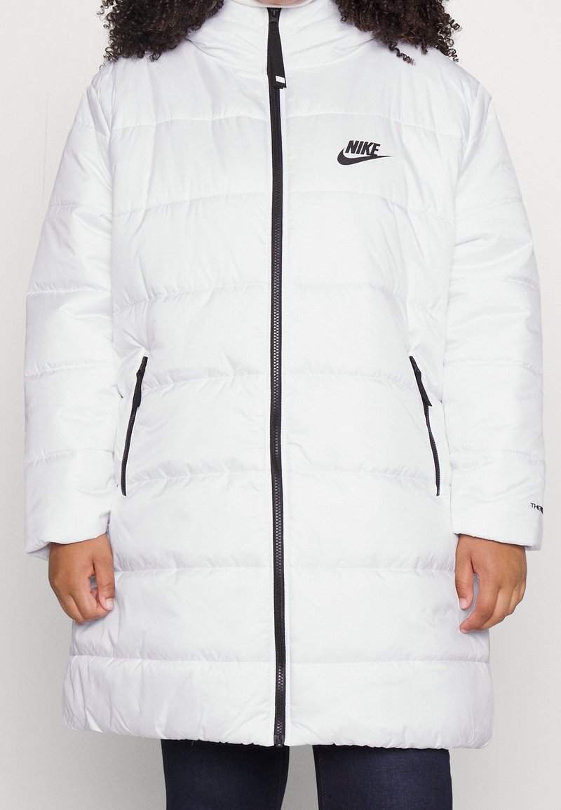 Biała kurtka puchowa z zamkiem z przodu, z poziomymi pikowanymi sekcjami i czarnym logo Nike. Posiada dwie boczne kieszenie oraz wysoki kołnierz.