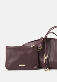 Sac à main en cuir bordeaux avec une fermeture éclair dorée, pochette détachable et texture lisse ; comprend une poignée tressée et des éléments en métal décoratifs.