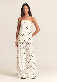 Weißer Stoff mit schwarzen Punkten; trägerloses Oberteil kombiniert mit weiten Hosen, glatte Textur, entspannte Passform und geschichtetes Design.