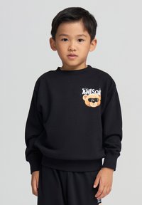 Sweatshirt nero con scollatura rotonda e polsini a costine, decorato con una grafica di un orso arancione con occhiali da sole e la scritta "AWESOME".