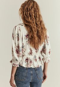 Blomstret bluse i hvid med lyserøde og blå mønstre, elastisk talje, pufærmer og blondekant. Sammen med højtaljede jeans.