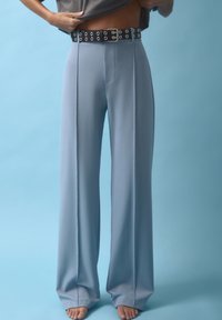 Hellblaue weit geschnittene Hosen mit glatter Textur, ausgestattet mit einem schwarzen Gürtel mit Metallösen und einer silbernen Schnalle.