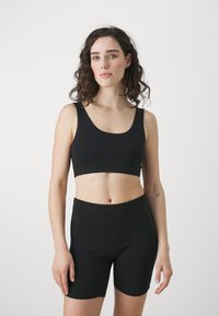 Crna sportska brusa i odgovarajuće visoke kratke hlače, bešavna izrada, rastezljiv materijal, uske forme, glatka tekstura, minimalistički stil.