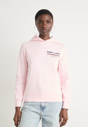 Sweat-shirt à capuche rose clair avec un logo sur le devant en bleu marine et rouge, des poignets côtelés et une coupe décontractée. Tissu en mélange de coton lisse.