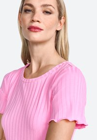 Haut rose à manches courtes avec texture côtelée, col rond et bords de manches froncés, composé d'un tissu lisse et léger.