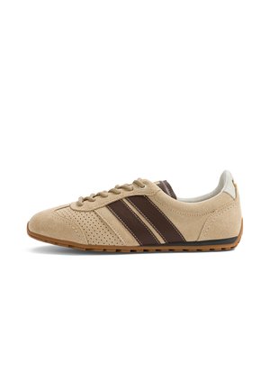 Baskets en daim beige avec bandes latérales en cuir marron, détails perforés, col blanc et semelle en gomme, vues de l'extérieur.