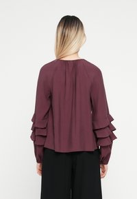 Pruimenblouse met gelaagde volantmouwen, ronde halslijn en geplooid detail aan de achterkant. Gemaakt van een gladde stof, met lange mouwen.
