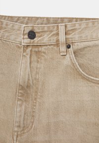Ceinture de jean en denim beige avec bouton noir, passant de ceinture, poche avant et détails de couture visibles.