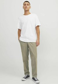 Weißes Baumwoll-T-Shirt mit Rundhalsausschnitt, kombiniert mit hellgrünen, schmal zulaufenden Hosen und marineblauen Segeltuchschuhen mit weißen Sohlen.