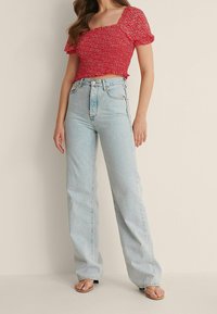 Rotes Blumen-Crop-Top mit kurzen Puffärmeln, kombiniert mit hellblauen, hochtaillierten, weit geschnittenen Jeans. Getragen mit beigen Flip-Flops.