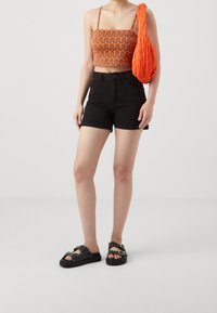 Oranssin kuvioitu crop-top lyhyillä ohuilla hihnoilla, mustat farkkushortsit ja mustat sandaalit, joissa hopeiset yksityiskohdat ja korotettu pohja.