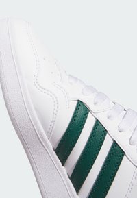 Białe sneakersy z zielonymi skórzanymi paskami i teksturowaną białą gumową podeszwą. Posiadają wyściełany język i oczka na sznurowadła.