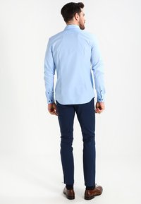 Lyseblå langermet skjorte med knapp-ned krage, buet søm og synlig søm, kombinert med marineblå slim-fit bukser og brune sko.