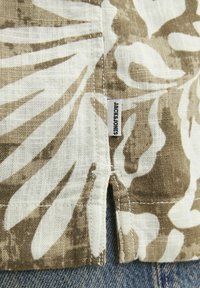 Trumpas rankovėmis marškiniai šviesiai rudos ir kremiškos gėlės rašto, pagaminti iš lengvos medžiagos, su šonine plyšio detalė ir etikete "JACK & JONES."