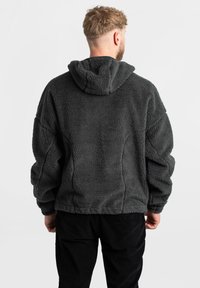 Felpa con cappuccio grigia in pile, con una consistenza morbida, vestibilità oversized e cappuccio. Presenta un design ampio e rilassato con dettagli di cucitura sottili.