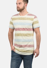 Tricou cu dungi, confecționat dintr-un material moale. Are o bază de crem deschis, cu dungi orizontale roșii, galbene și albastre, și un guler tip crew ribburat.