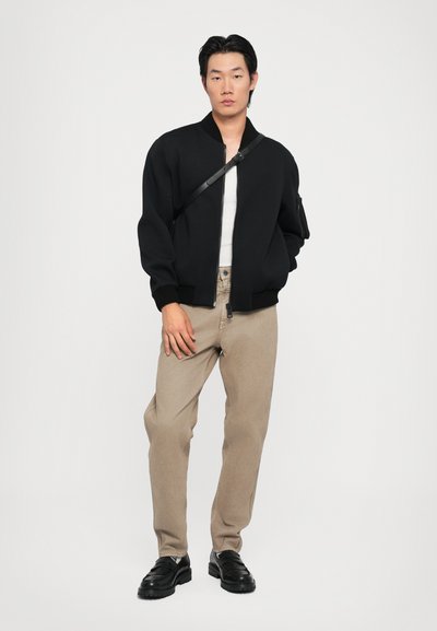 Sort bomberjakke, solid strikketekstur, lynlås lukning, parret med lyse beige bukser og sorte sko, minimalistisk design og farveskema.