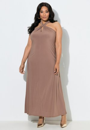 Mujer con cabello largo y oscuro, vistiendo un vestido maxi sin mangas color malva con cuello halter y tacones dorados puntiagudos, posando frente a un fondo blanco.