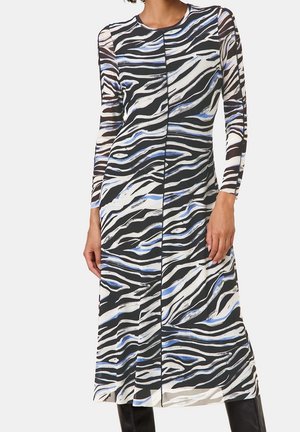 Jurk met lange mouwen met zwart, wit en blauw zebraprintpatroon, getailleerd en tot halverwege de kuit vallend, gedragen met zwarte laarzen.
