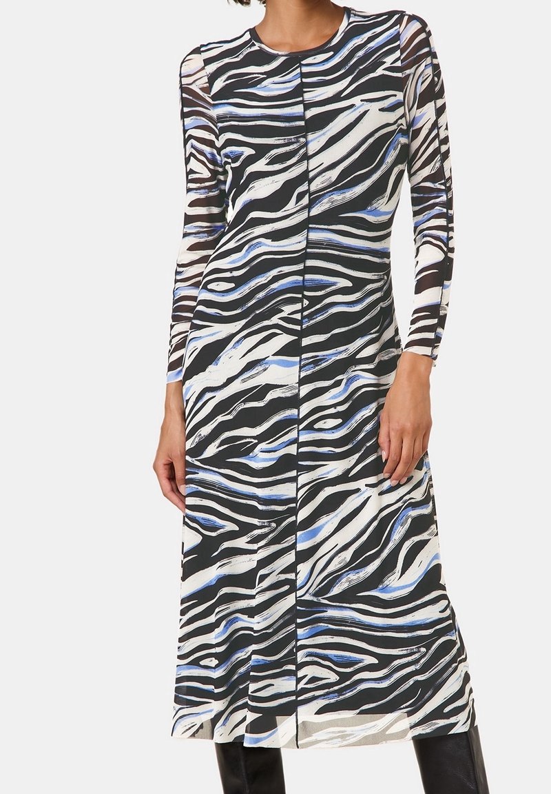 Robe à manches longues avec motif zèbre noir, blanc et bleu, cintrée à la taille et arrivant au milieu du mollet, portée avec des bottes noires.