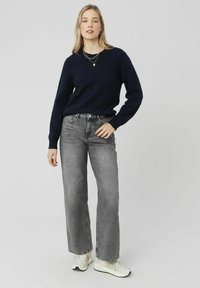 Pull en tricot bleu marine à manches longues, associé à un jean gris délavé taille haute et des baskets blanches. Colliers superposés simples.