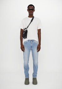 White cotton t-shirt, light blue denim jeans, black crossbody bag with silver hardware, gray-green clogs, and dark sunglasses.