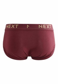 Shorts maroon avec une texture lisse et une large ceinture arborant "NEXT" en lettres dorées. Le design est minimaliste et ajusté.