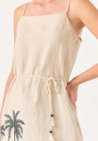 Beige linnen jurk met een vierkante halslijn, verstelbare spaghetti-bandjes, een trekkoord in de taille en een palmboomprint met decoratieve kralen.