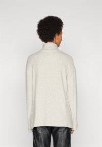 Light gray, oversized turtleneck sweater with a soft texture, drop shoulders, and side slits. Paired with black, loose-fitting leather pants.