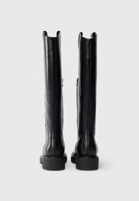 Une paire de bottes en cuir noires hautes, debout sur un fond blanc uni, vues de l'arrière.