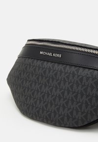 Sac banane en tissu noir avec un motif monogramme MK texturé et un accent en cuir lisse. Comprend une fermeture éclair et une plaque logo de la marque.
