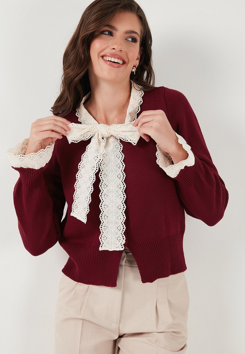 Burgundský pletený svetr s bílým krajkovým lemem, s mašlí na límci a rozšířenými rukávy. Měkký materiál, zkrácený střih.