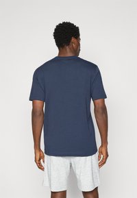 Marineblaues Baumwoll-T-Shirt mit kurzen Ärmeln, Rundhalsausschnitt und glatter Textur, getragen mit hellgrauen Shorts.