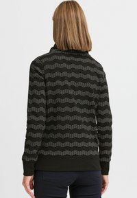 Fekete pulóver zigzag fehér mintával, bordázott mandzsettákkal és szegéllyel. Magas nyakkivágással és puha, texturált anyagból készült.