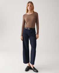 Woman wearing brown ribbed long-sleeve top, black belt, dark blue wide-leg jeans, and black loafers against plain light background.