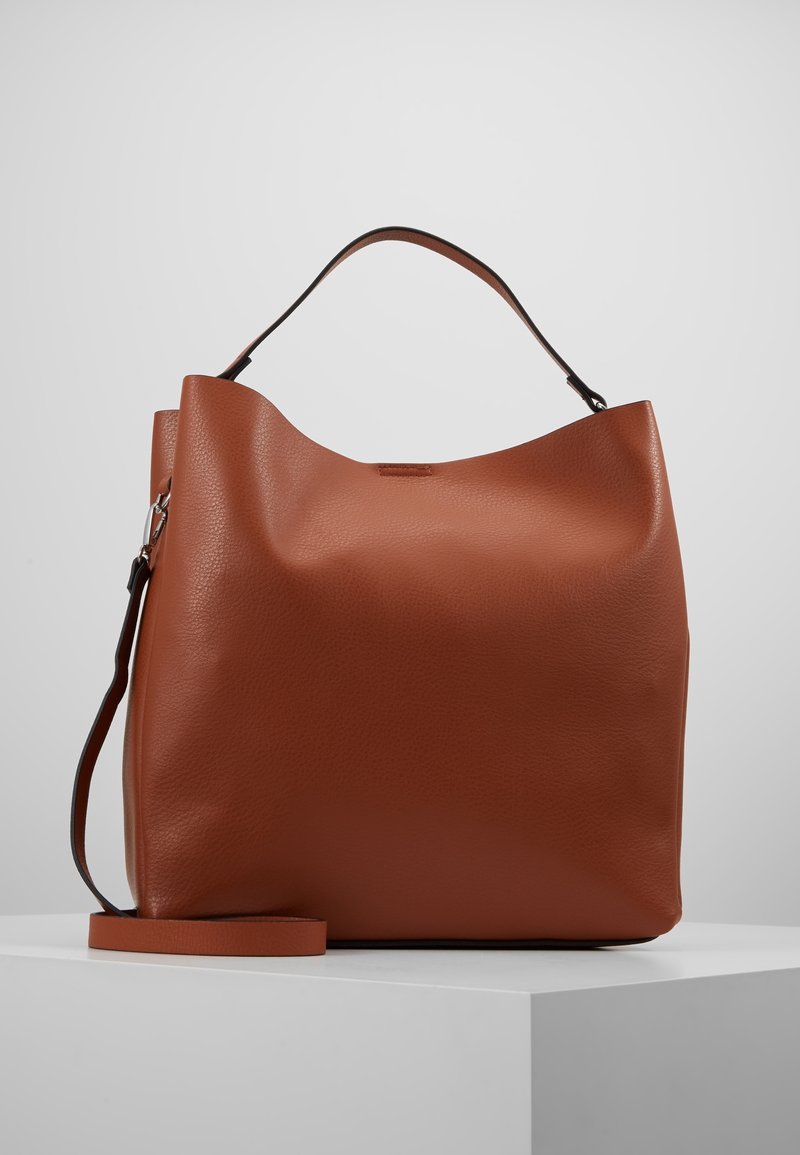 Sac à main en cuir marron avec une seule anse supérieure et une longue bandoulière amovible, présenté sur un socle blanc avec un fond uni.