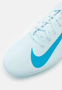 Bota de fútbol color azul claro con superficie texturizada, que presenta un prominente swoosh de Nike en color turquesa, cordones planos y un diseño aerodinámico.