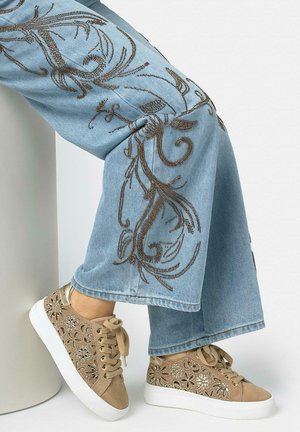 Vaqueros anchos de color azul claro con bordado marrón intrincado, combinados con zapatillas beige con recortes florales y suelas blancas.