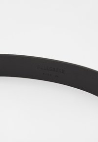 Sorte bælte med en glat tekstur, mærket "Pull&Bear," og markeret med størrelsen "85" på indersiden. Enkel, slank design.