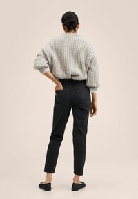 Suéter de punto gris claro, jeans negros de cintura alta y planos negros; diseño minimalista con un corte holgado y tejido texturizado.