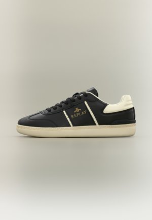 Baskets noires avec des accents crème, dessus en cuir texturé, bout arrondi et lacets plats. Présente un logo détaillé sur le côté et le talon.