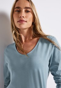 Light blue long-sleeve top with a V-neck design. Soft fabric with a smooth texture, featuring fitted sleeves and a simple silhouette.