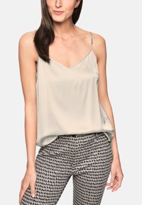 Light gray camisole with a V-neck and thin straps, paired with high-waisted trousers featuring a dark polka dot pattern on a light background.