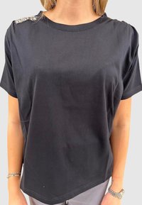 Sort bomulds t-shirt med rund halsudskæring og korte ærmer, med dekorative detaljer på venstre skulder og en afslappet pasform.